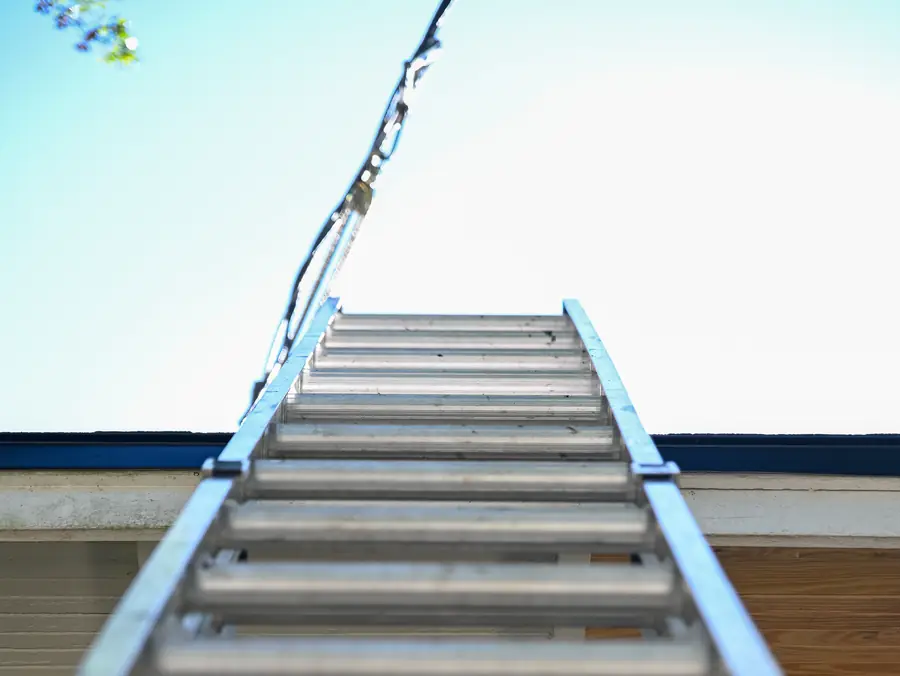 Aluminum extension ladder leaning against a roof edge under a clear blue sky