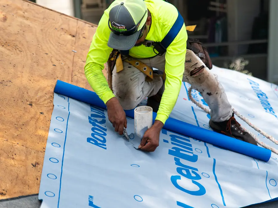 Gold Key roofer cutting new underlayment around a plumbing vent pipe on a roof deck