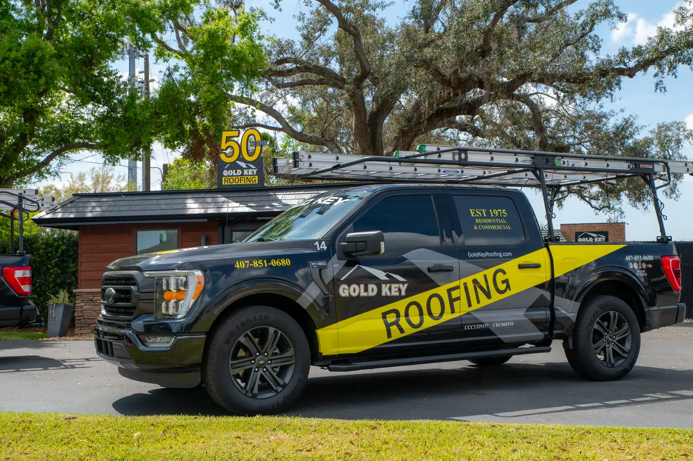 A black Gold Key Roofing truck parked at the office beneath the company’s 50 year sign