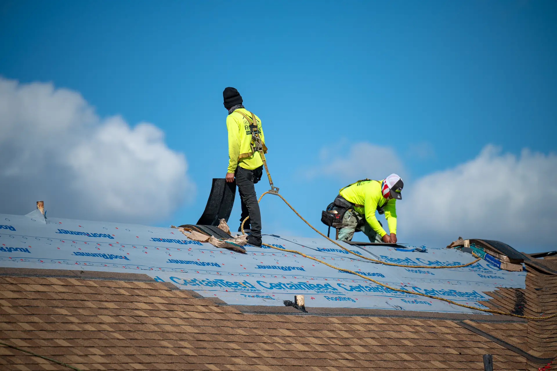 Two Gold Key Roofing crew members at work on a roof under a blue sky