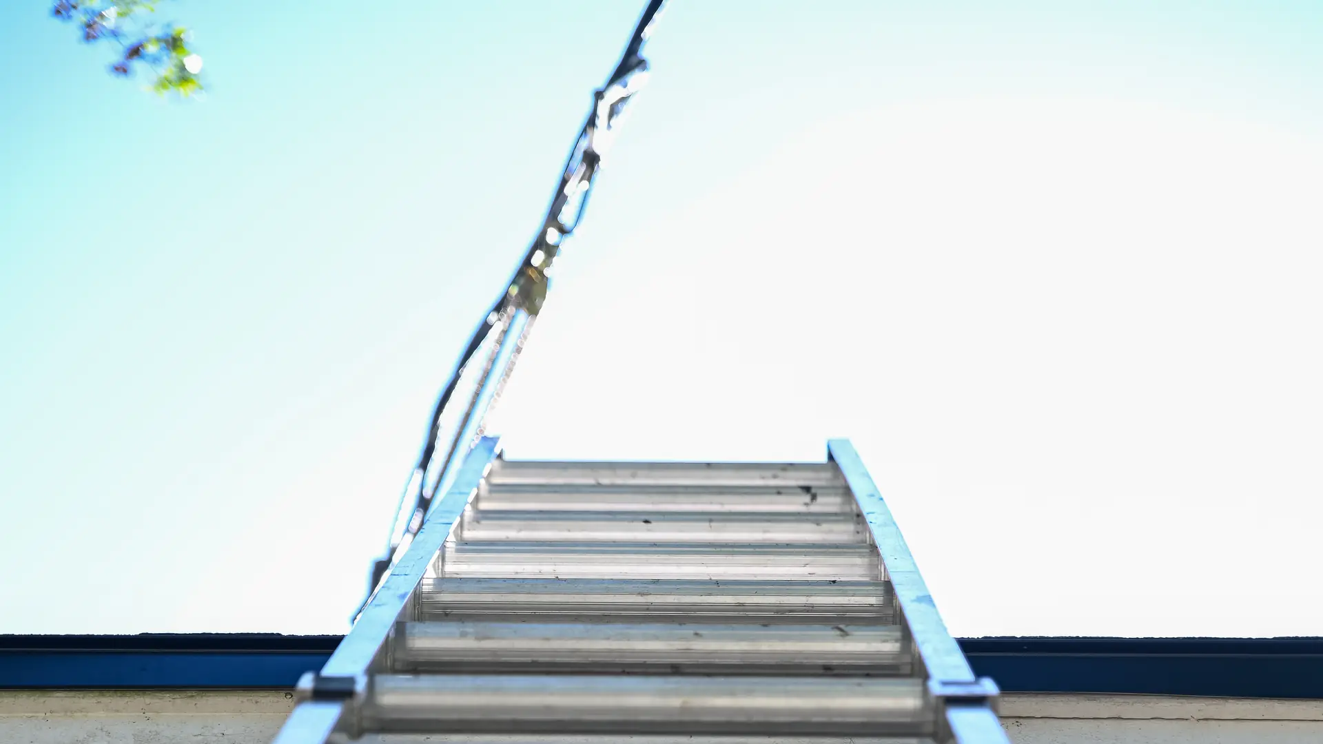 Aluminum extension ladder leaning against a roof edge under a clear blue sky