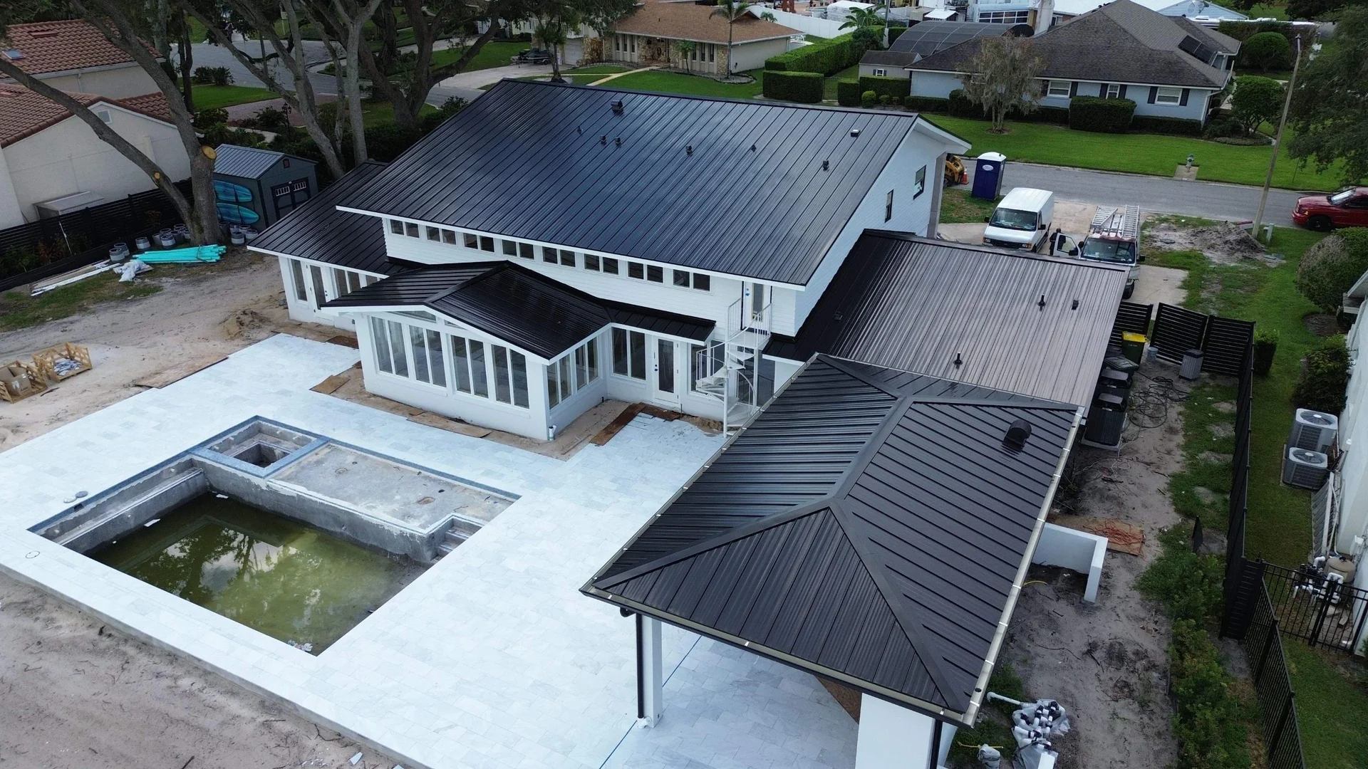Black standing seam metal roof on a two story white home with a pool deck, seen from the air