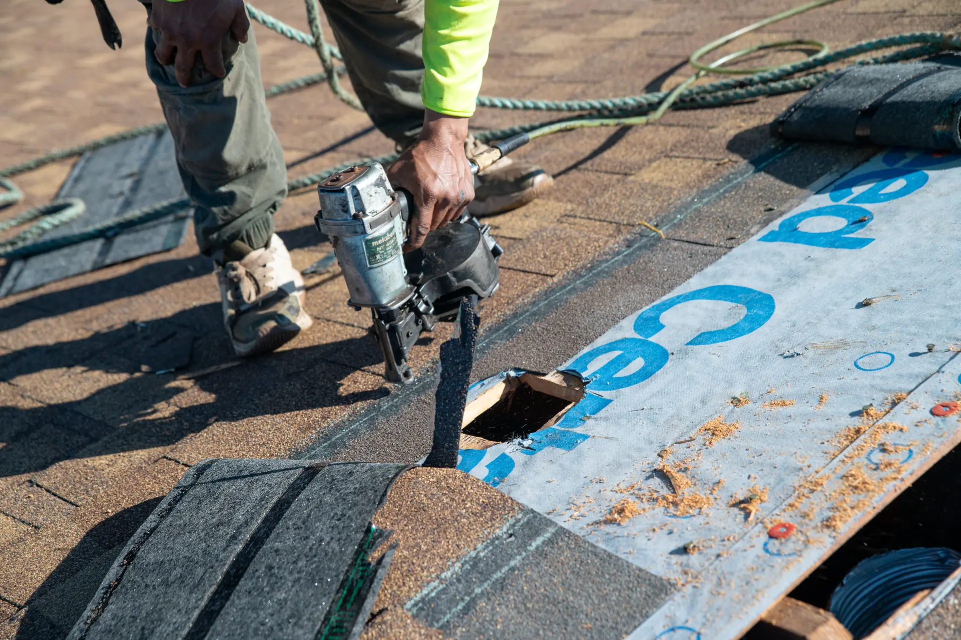 Gold Key roofer with a nail gun beside an opening in the roof deck, with new underlayment and shingles around it
