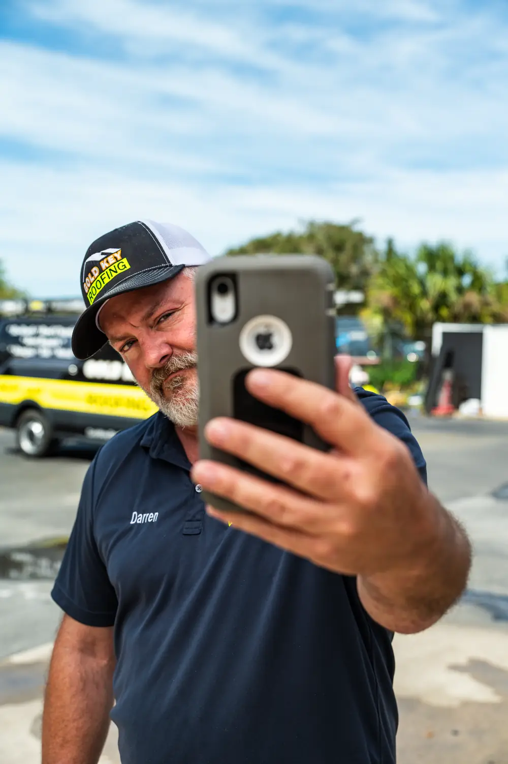 Gold Key team member taking a photo with his phone beside the company’s roofing trucks