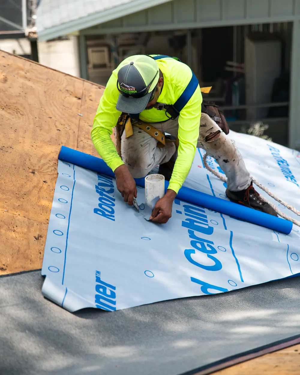 Gold Key roofer cutting new underlayment around a plumbing vent pipe on a roof deck