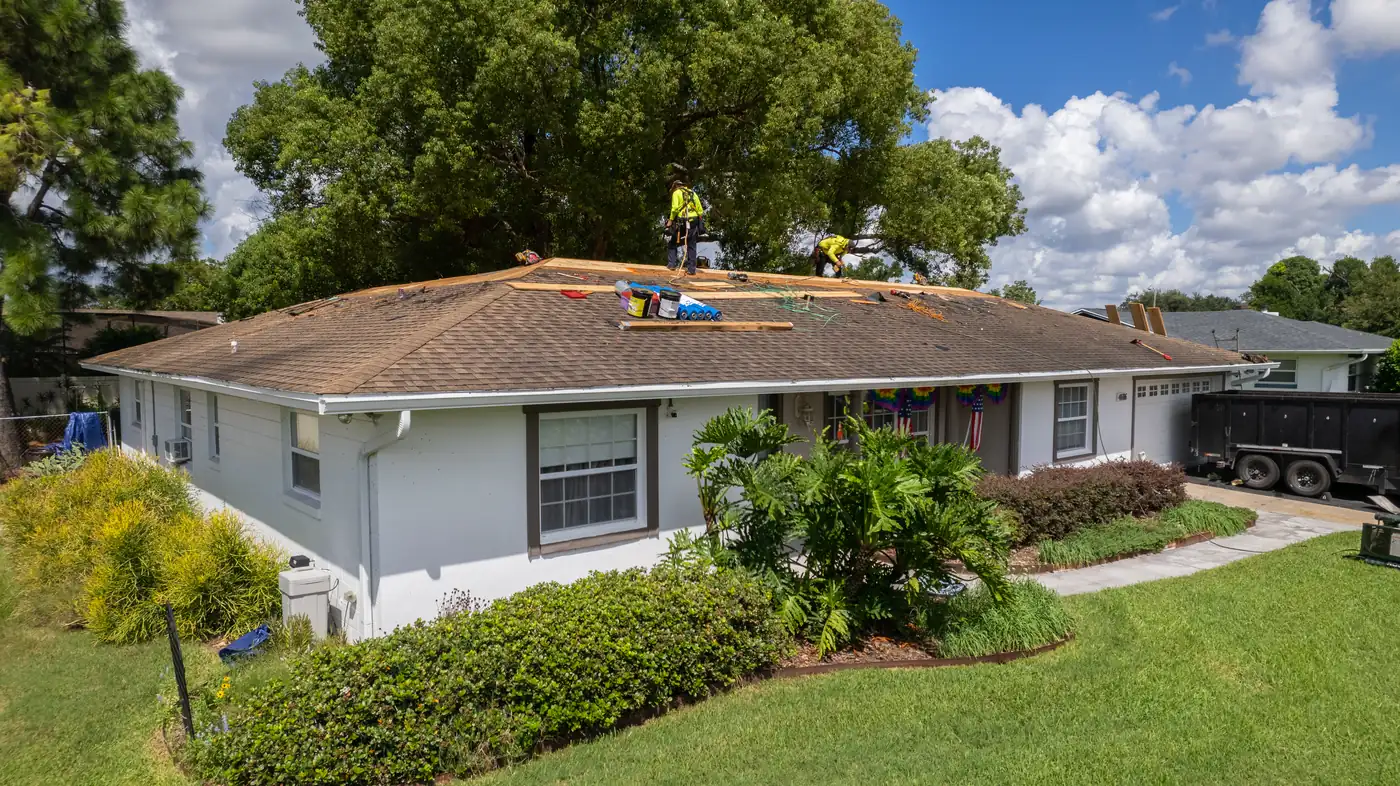 Crew installing new decking on a white ranch home with a dump trailer in the driveway