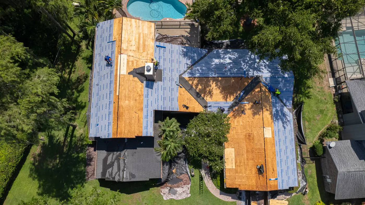 Aerial view of a home partway through a roof replacement, with new plywood decking and synthetic underlayment