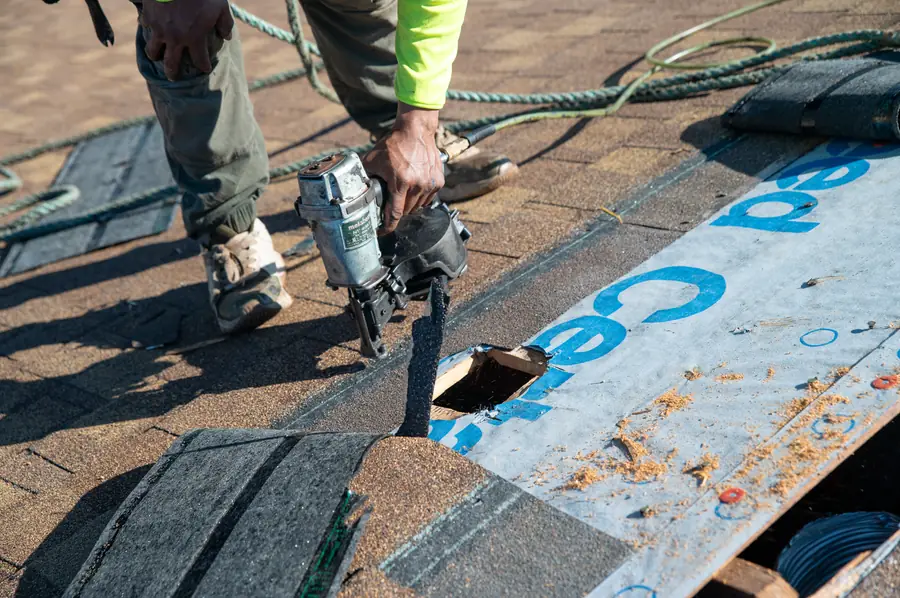 A Gold Key roofer nailing shingles over new underlayment, seen up close