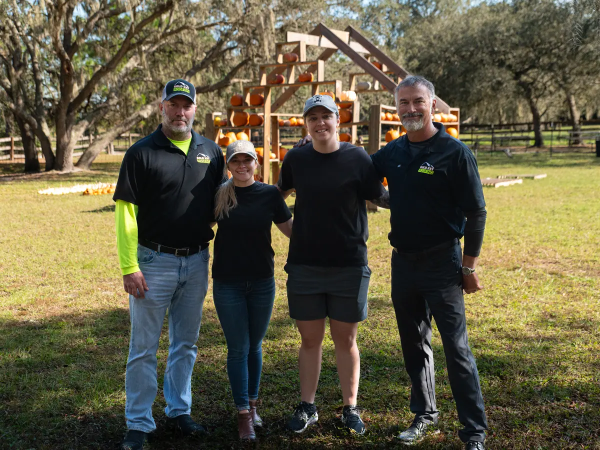 Four Gold Key Roofing team members standing together on a lawn in front of a pumpkin display