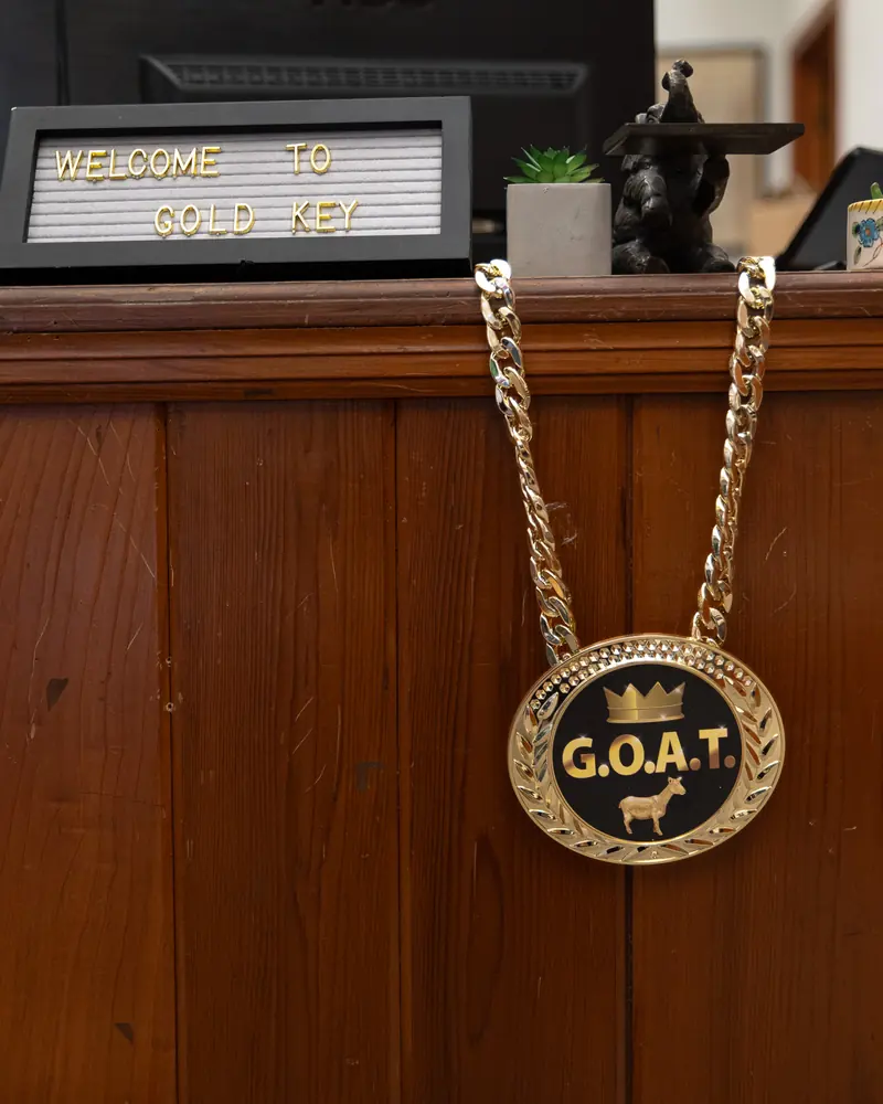 A gold G.O.A.T. medal hanging from the welcome sign on the office front desk