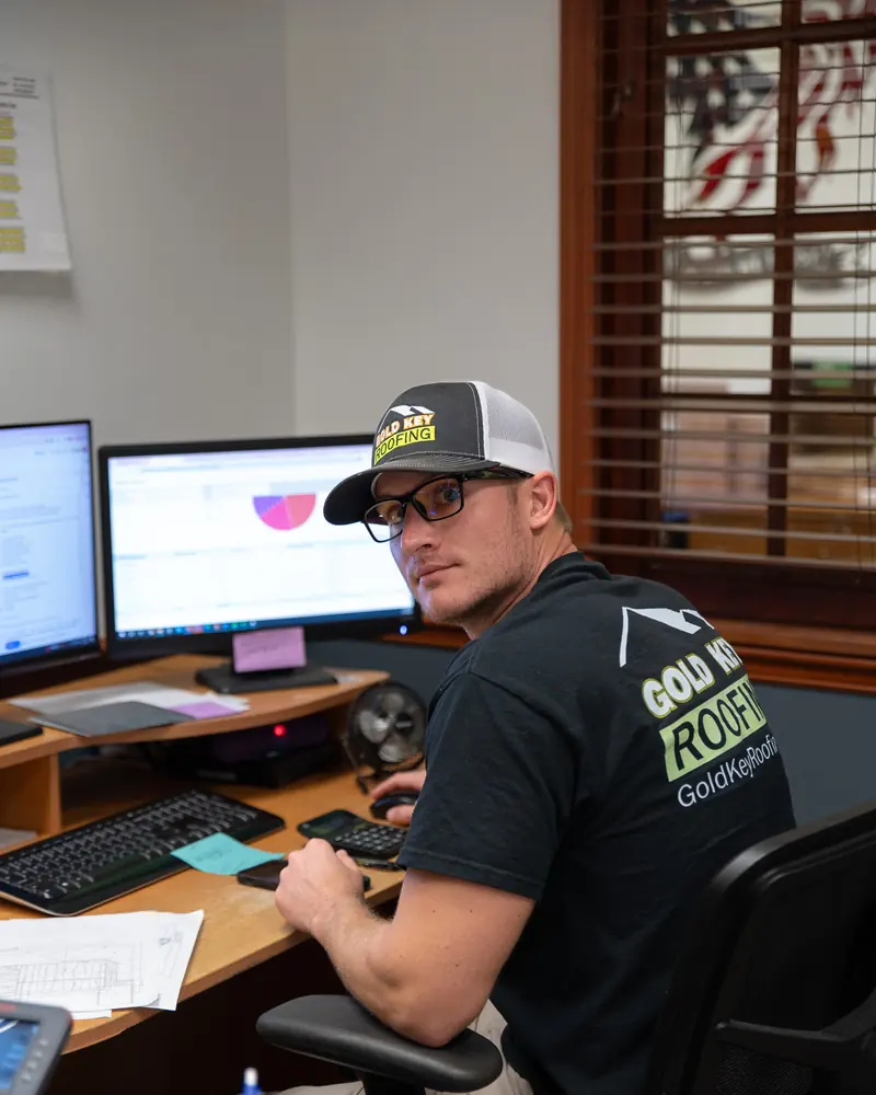 A Gold Key Roofing team member smiling at his desk in the office
