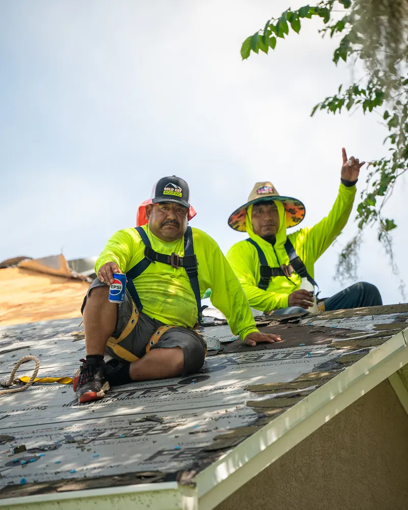 Two roofers taking a break on a roof, one waving at the camera