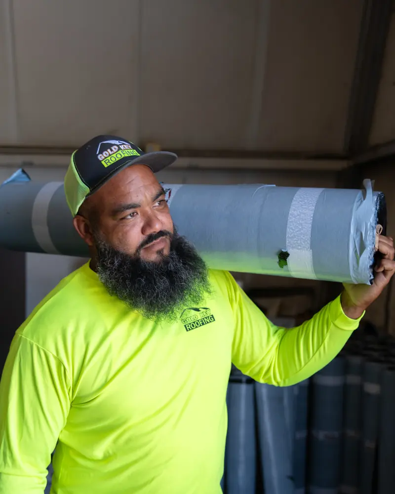 A crew member carrying a roll of roof underlayment on his shoulder in the warehouse