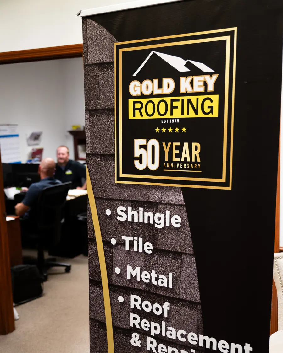 Gold Key Roofing 50 year anniversary banner listing shingle, tile and metal roofing in the office